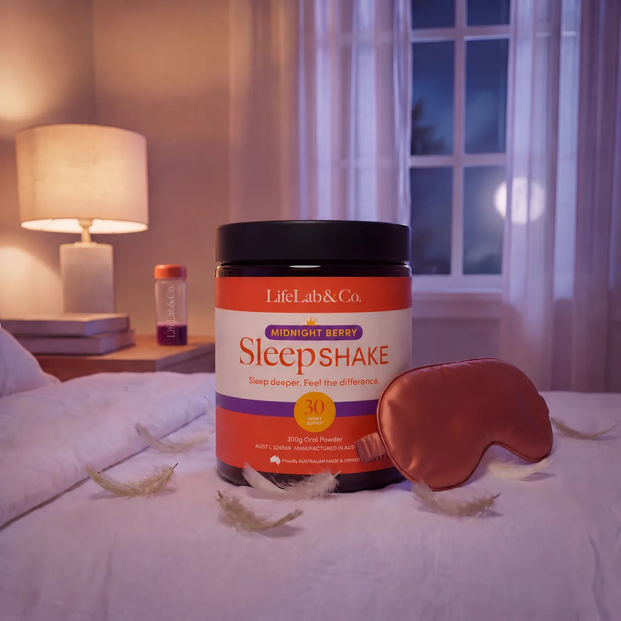 SleepSHAKE Midnight Berry jar on a bed beside a satin eye mask, with a shaker and lamp on the bedside table at night